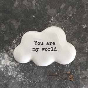 Pode incluir: Um prato de cerâmica branco em forma de nuvem com o texto "You are my world" em preto. O prato está sobre uma superfície escura e texturizada, com um pequeno ramo de matéria vegetal seca por perto.