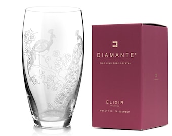 Puede incluir: Un vaso de cristal transparente con un diseño de pavo real grabado, junto a una caja burdeos. El vaso presenta dos pavos reales posados en una rama florecida. La caja dice "Diamante Fine Lead Free Crystal" y "Elixir Collection".