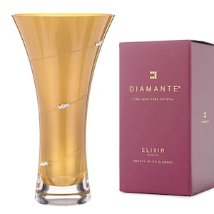 Puede incluir: Un jarrón de vidrio dorado con una base transparente y un patrón de diamante. El jarrón está decorado con pequeños cristales transparentes. El jarrón está sobre una superficie blanca. El texto en la caja dice "Diamante Fine Lead Free Crystal Elixir Collection Beauty in its Element".