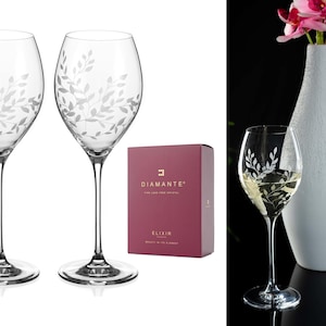 Peut inclure: Deux verres à vin en verre transparent avec un motif floral gravé. Les verres sont sur une surface blanche. Une boîte avec le texte "Diamante Elixir" est en arrière-plan.
