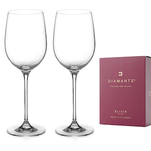 May include: Two clear glass wine glasses with a tall, slender stem and a wide bowl. The glasses are on a white background. A red box with gold lettering reads "DIAMANTE Fine Lead Free Crystal Elixir Collection Beauty in its Element"