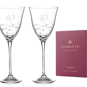 May include: Two clear glass wine glasses with a 40th anniversary design. The glasses feature a silver swirl design with small crystal accents. The glasses are in front of a red box with the words "Diamante Fine Lead Free Crystal Elixir Collection Beauty in its Element" printed on it.