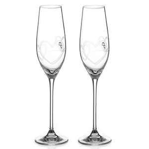 May include: Two clear glass champagne flutes with etched heart designs. The flutes have a long stem and a wide bowl.