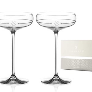 May include: Two clear glass champagne flutes with a silver band and the number 18 etched on the side. The flutes are in a white box with a silver pattern and the word "Diamante" printed on the front.