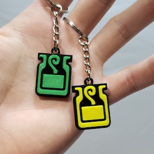May include: Two keychains with black metal rings and chains. The charms are black with green and yellow potion bottles with swirling steam.