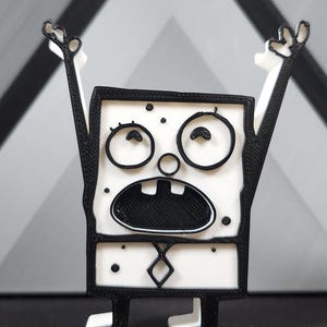 Op de afbeelding: Een zwart-wit 3D-geprint beeldje van een cartoonfiguur met een verraste uitdrukking. Het personage heeft grote ogen, een brede mond en draagt een stropdas.