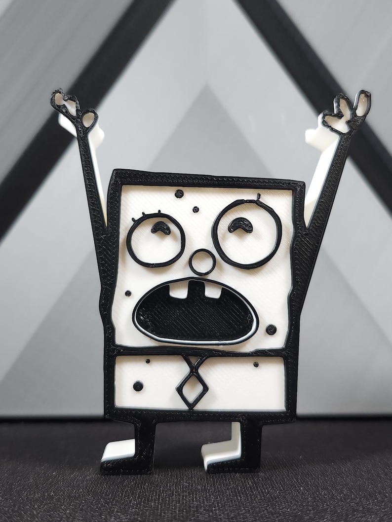 Op de afbeelding: Een zwart-wit 3D-geprint beeldje van een cartoonfiguur met een verraste uitdrukking. Het personage heeft grote ogen, een brede mond en draagt een stropdas.