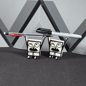 Op de afbeelding: Twee zwart-witte cartoonfiguren die een zwart-witte marker en een rode pen vasthouden. De figuren staan op een grijs oppervlak.