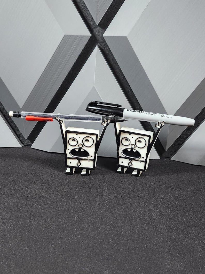 Op de afbeelding: Twee zwart-witte cartoonfiguren die een zwart-witte marker en een rode pen vasthouden. De figuren staan op een grijs oppervlak.