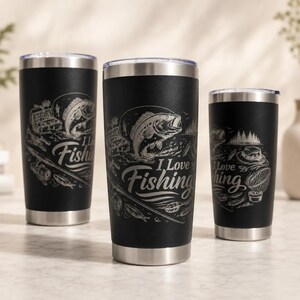 Op de afbeelding: Drie zwarte roestvrijstalen bekers met zilveren randen en bodems. Elke beker heeft een thema over vissen, met afbeeldingen van vissen, visgerei en de tekst "I Love Fishing" of "Fishing".