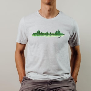 May include: A light gray t-shirt with a watercolor design of a forest reflected in a lake. The text "felt" is written in black below the design.