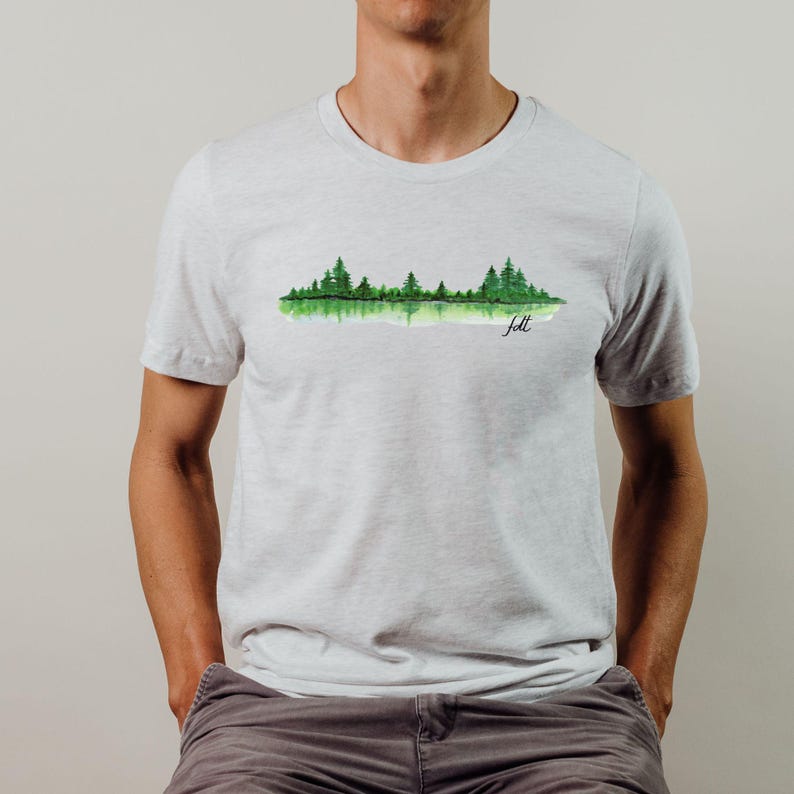 May include: A light gray t-shirt with a watercolor design of a forest reflected in a lake. The text "felt" is written in black below the design.