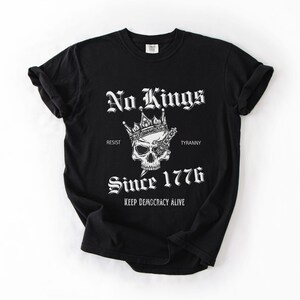 Może przedstawiać: Czarna koszulka z białym nadrukiem przedstawiającym czaszkę w koronie z mieczem. Tekst: "No Kings", "Resist", "Tyranny", "Since 1776" i "Keep Democracy Alive".