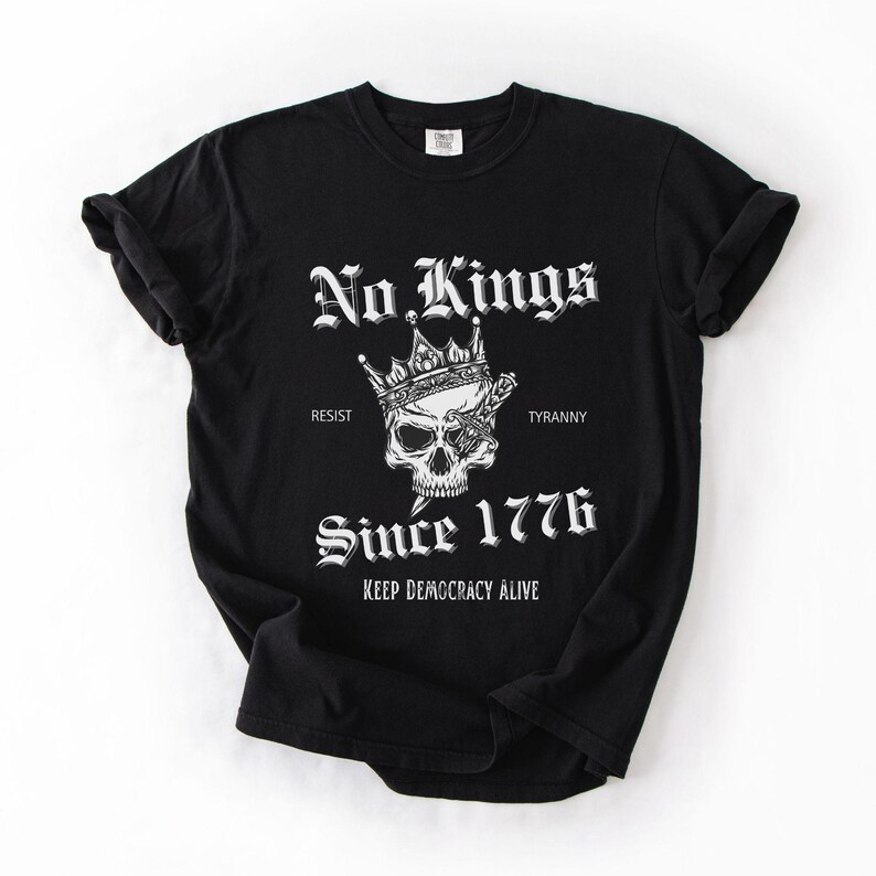 Może przedstawiać: Czarna koszulka z białym nadrukiem przedstawiającym czaszkę w koronie z mieczem. Tekst: "No Kings", "Resist", "Tyranny", "Since 1776" i "Keep Democracy Alive".