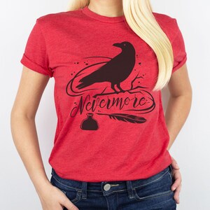 May include: Red t-shirt with a black silhouette of a raven perched on a branch. The text "Nevermore" is written in a stylized font below the raven. A quill pen and inkwell are also included in the design.