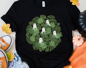 May include: Black t-shirt featuring a graphic of white ghosts in a circle of green monstera leaves.