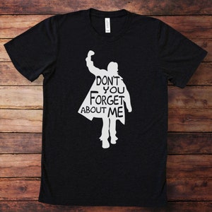 Puede incluir: Camiseta negra con una silueta blanca de una persona con el pu&ntilde;o en alto y el texto "Don't you forget about me".