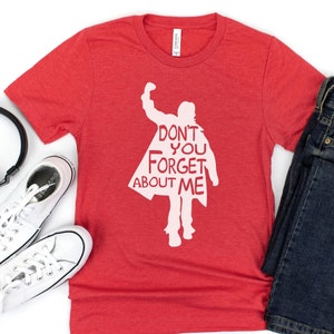 Puede incluir: Camiseta roja con una silueta blanca de una persona con el texto "Don't you forget about me" impreso en ella.