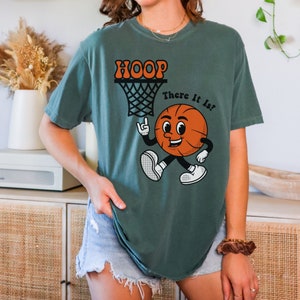 May include: A teal green t-shirt with a basketball graphic and the text "HOOP There It Is!" printed on the front.
