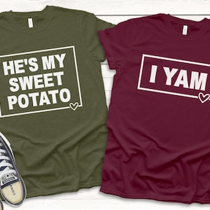 May include: Two t-shirts with a matching couple's design. One shirt is olive green with the text "He's my sweet potato" in a white box. The other shirt is burgundy with the text "I yam" in a white box.