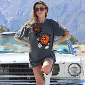 May include: A charcoal grey t-shirt with a cartoon basketball graphic and the text "HOOP There It Is!"