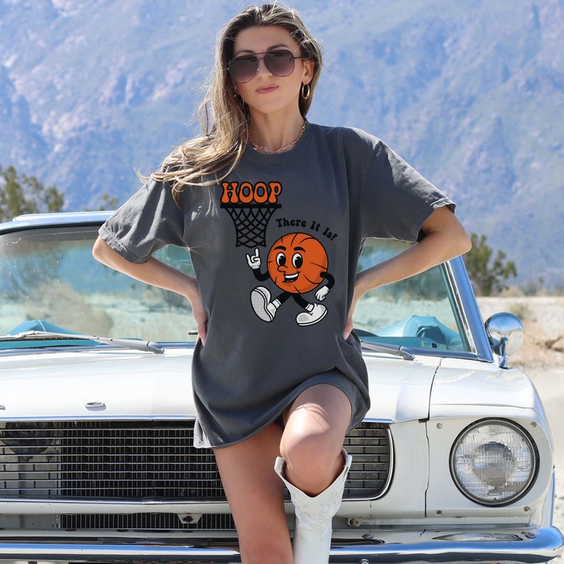May include: A charcoal grey t-shirt with a cartoon basketball graphic and the text "HOOP There It Is!"