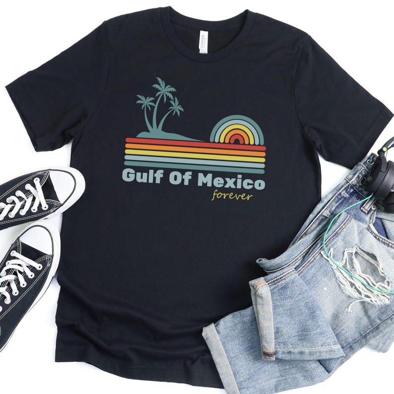 Pu&ograve; includere: Maglietta nera con una grafica retr&ograve; di palme e un tramonto su uno sfondo a righe. Il testo "Gulf of Mexico forever" &egrave; stampato sotto la grafica.