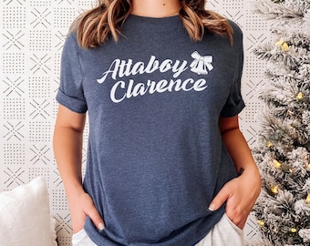 May include: A navy blue t-shirt with white text that reads "Attaboy Clarence" and a white illustration of a bow and bells.