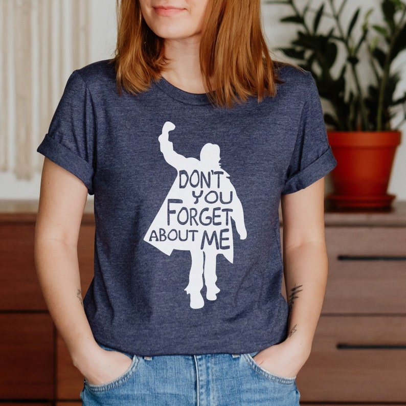 Puede incluir: Una camiseta azul marino con una silueta blanca de una persona con el texto "Don't you forget about me" impreso en ella.