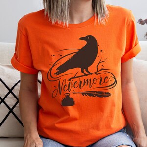 May include: Orange t-shirt with a black raven silhouette, a quill pen, and an ink bottle. The text "Nevermore" is written in a stylized font.