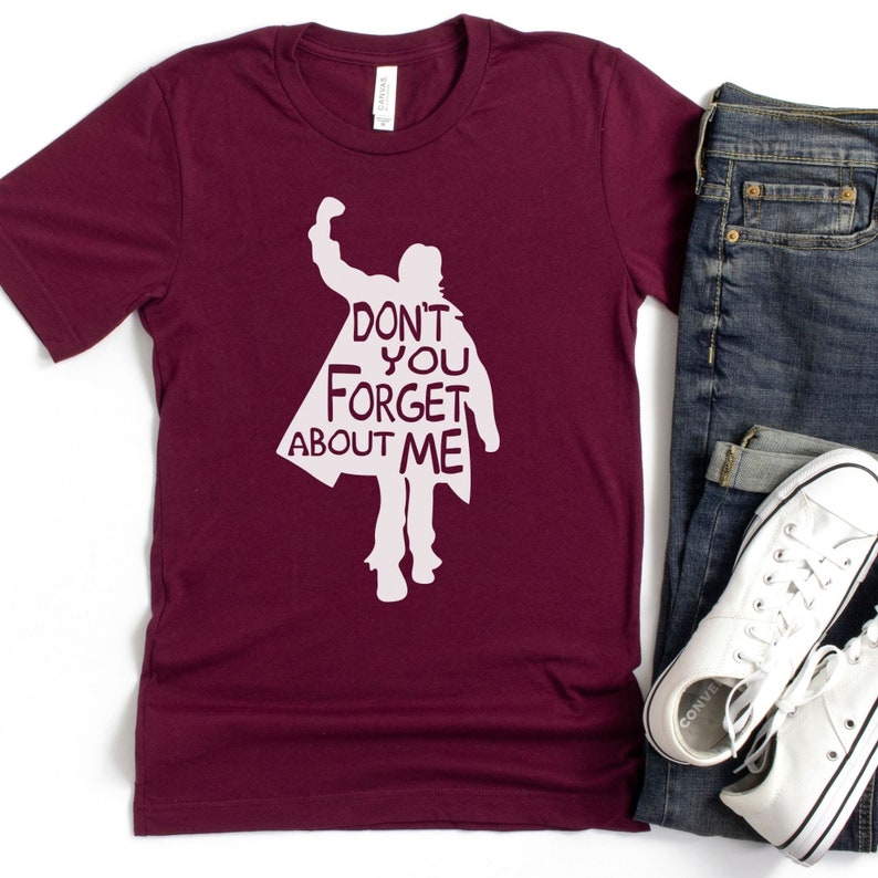 Puede incluir: Una camiseta de color granate con una silueta blanca de una persona con el texto "Don't you forget about me" impreso en la parte delantera.