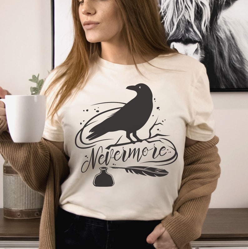 May include: A white t-shirt with a black raven illustration and the text "Nevermore" in a stylized font. The raven is perched on a branch with a quill pen and inkwell below.