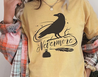 May include: A yellow t-shirt with a black silhouette of a raven perched on a branch. The text "Nevermore..." is written in a stylized font below the raven. A black inkwell and quill are also depicted.