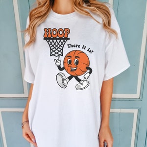 May include: White t-shirt with a cartoon basketball graphic and the text "HOOP There It Is!"