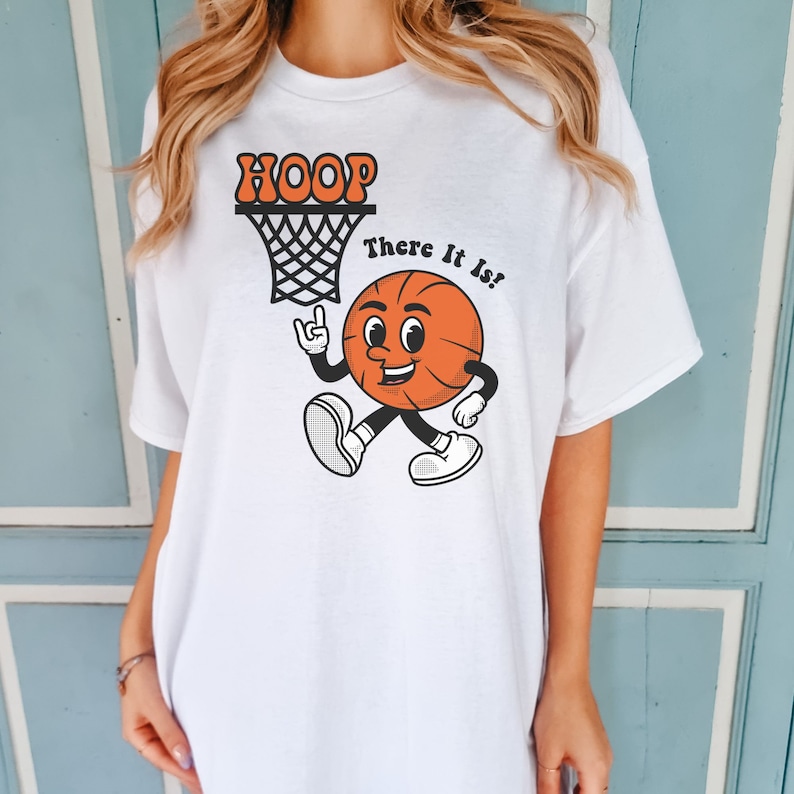 May include: White t-shirt with a cartoon basketball graphic and the text "HOOP There It Is!"