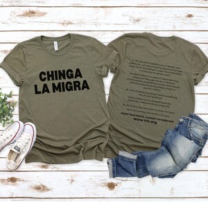 May include: Olive green t-shirts with black text. One shirt reads "CHINGA LA MIGRA" and the other has text about constitutional rights. A pair of blue jeans and white sneakers are also in the image.
