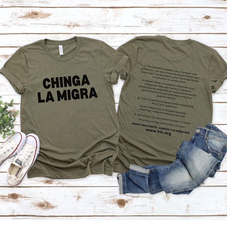 May include: Olive green t-shirts with black text. One shirt reads "CHINGA LA MIGRA" and the other has text about constitutional rights. A pair of blue jeans and white sneakers are also in the image.