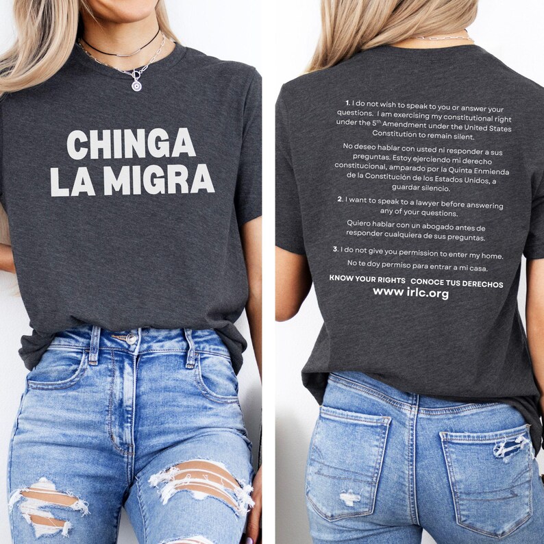 May include: Dark gray t-shirt with the text "CHINGA LA MIGRA" in white. The back of the shirt has text in English and Spanish about constitutional rights. The shirt is paired with blue jeans.