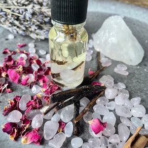 Könnte beinhalten: Eine kleine Glasflasche mit schwarzem Verschluss, gefüllt mit einer klaren Flüssigkeit und verschiedenen Pflanzen. Die Flasche ist umgeben von rosa Rosenblüten, weißen Quarzkristallen und Zimtstangen.