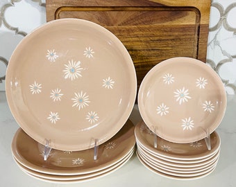 May include: A set of vintage pink and white floral dinnerware with a daisy pattern. The set includes a large platter, a smaller serving dish, and six smaller plates.