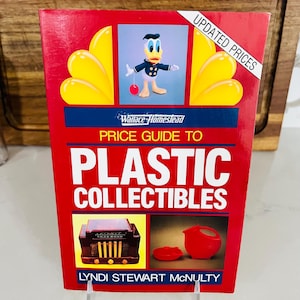 May include: A red book titled "Price Guide to Plastic Collectibles" by Lyndi Stewart McNulty. The cover features a cartoon of Donald Duck, yellow accents, and images of plastic collectibles.