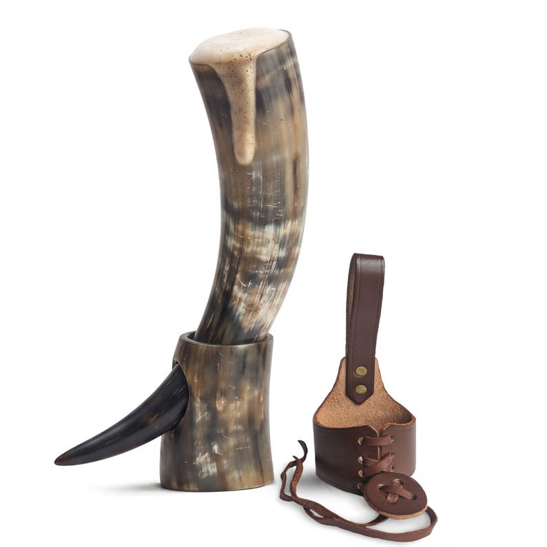May include: A curved drinking horn with a natural mottled brown and cream finish, resting in a matching horn stand with a pointed side protrusion. Beside it sits a brown leather belt holster featuring a lace-up design and a vertical strap.
