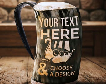 May include: A horn-shaped mug filled with beer, featuring a dark handle and a base. The mug has the text "YOUR TEXT HERE" and "CHOOSE A DESIGN" with a Viking ship graphic. The mug sits on a wooden surface.