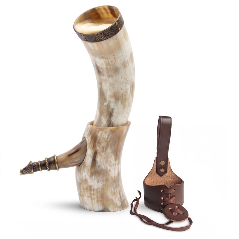 May include: A curved drinking horn with a natural cream and brown mottled finish, featuring a metallic rim with intricate embossed patterns and a pointed metal tip. Beside it sits a brown leather holster with a lace-up design and a belt loop.