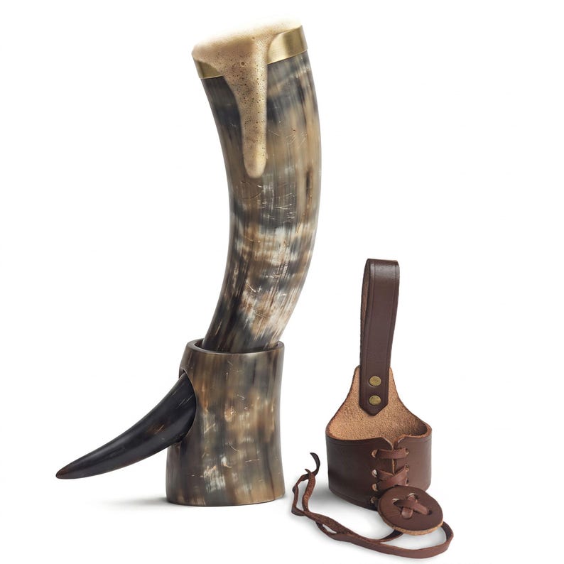 May include: A curved drinking horn with a polished brass rim and a natural mottled brown and cream finish, resting in a matching horn stand. Beside it sits a brown leather belt holster featuring a lace-up design with brass rivets and a cord.