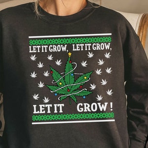Puede incluir: Sudadera negra con una hoja de cannabis decorada como un árbol de Navidad. El diseño incluye el texto "LET IT GROW, LET IT GROW, LET IT GROW!" y hojas de cannabis blancas. La sudadera tiene un borde con estampado verde y blanco.