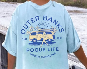 May include: Light blue t-shirt featuring a graphic of a vintage van with a surfboard on top and the text "Outer Banks Sand Surf Pogue Life North Carolina".
