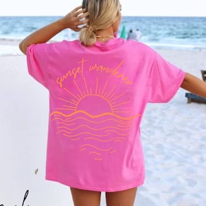 May include: Pink t-shirt with a sunset and waves graphic and the text "sunset wanderer" on the back.