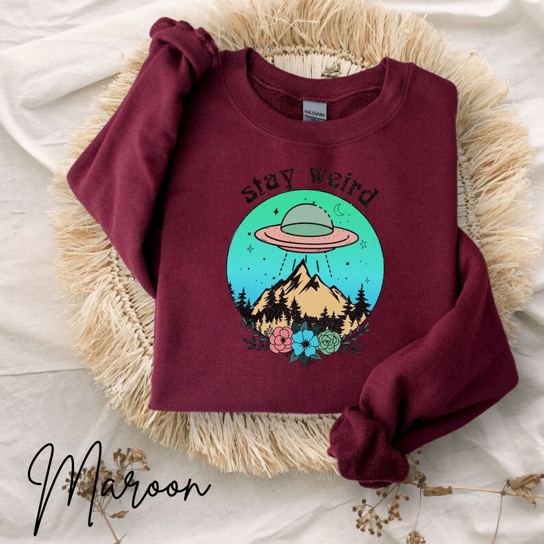 May include: Maroon sweatshirt with a graphic of a UFO over a mountain range with the text "stay weird" in a circle.