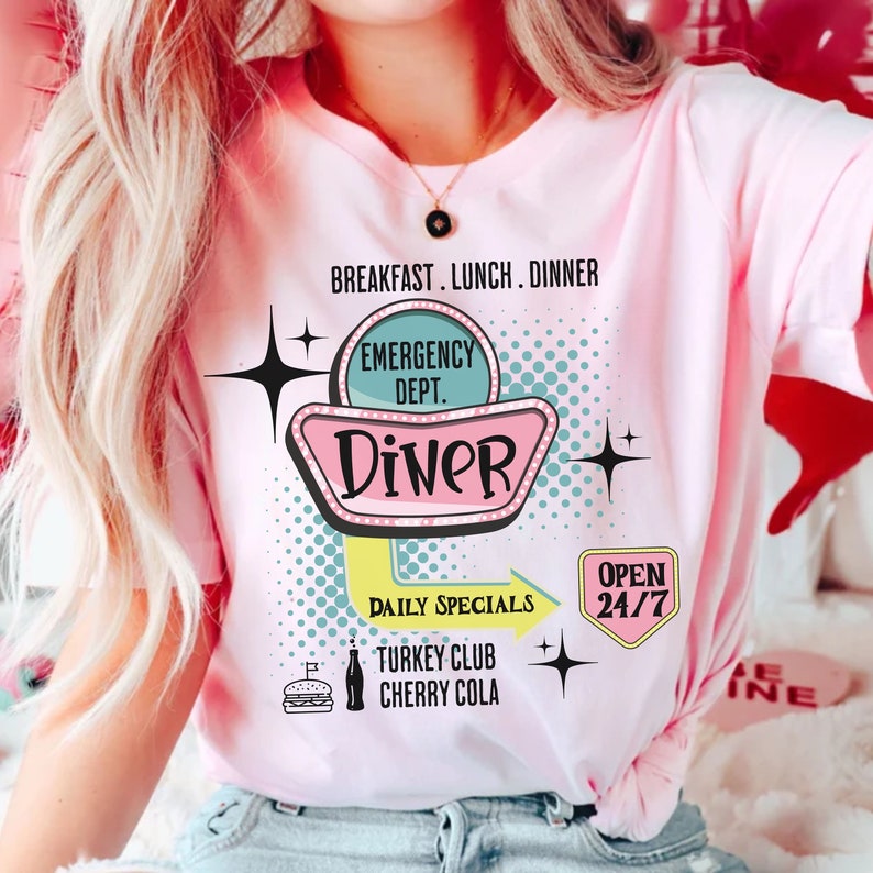 以下が含まれることがあります： レトロなダイナーのデザインが特徴のピンクのTシャツ。「Diner」の文字がヴィンテージ風の看板スタイルで描かれ、「Breakfast, Lunch, Dinner」、「Daily Specials」、「Open 24/7」の文字も含まれています。ハンバーガーとコーラも描かれています。